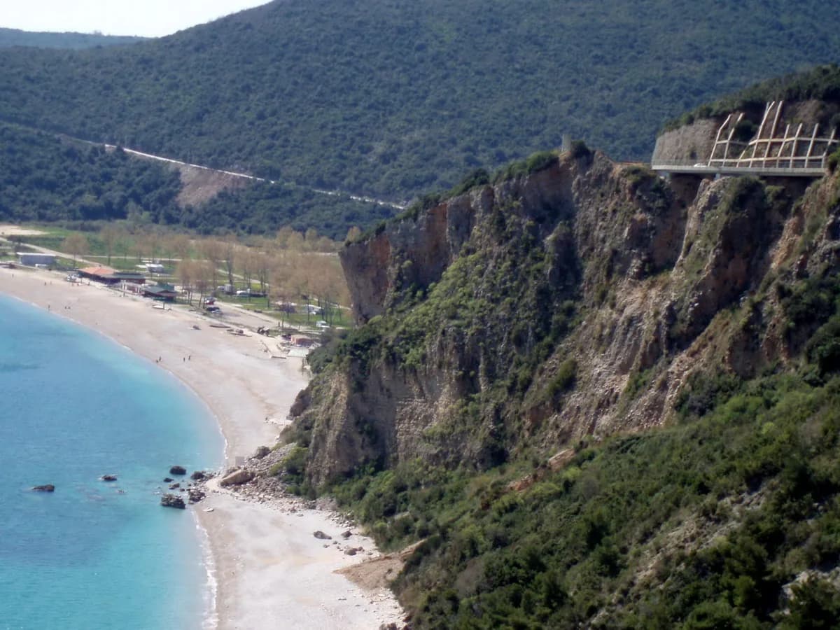 A view of Jaz Beach, turquoise water and the coastal road through the hills